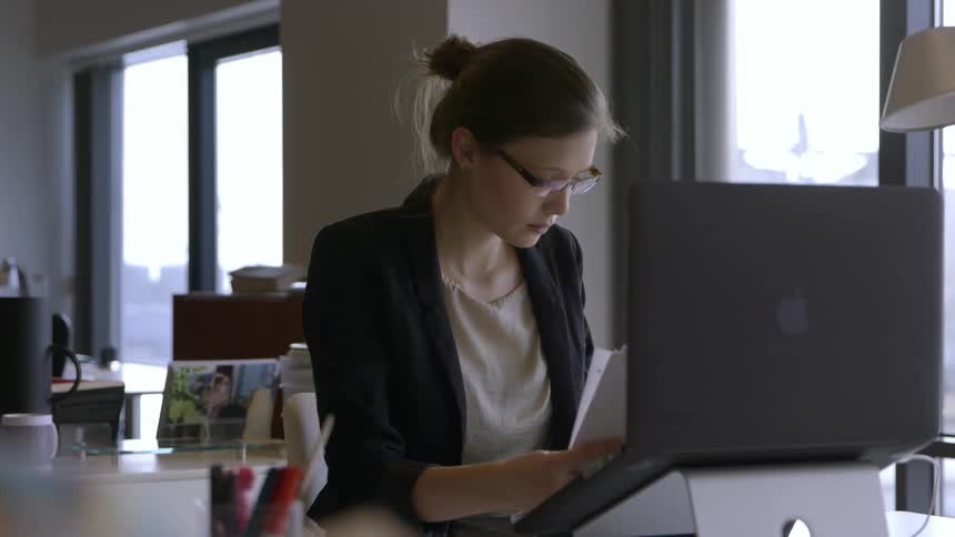 A woman using a computer puts papers in a notebook