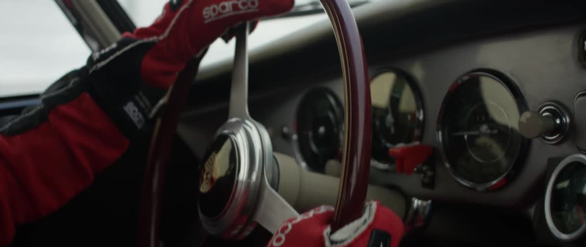 A race car driver's gloved hands are shown gripping the wheel while they drive