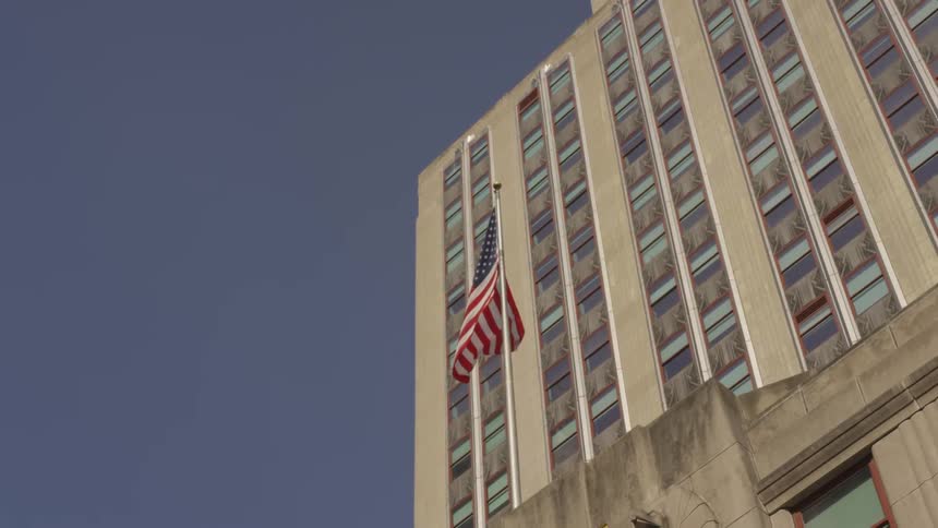 The american flag is billowing in the wind as it hangs from a lone flagpole atop a concrete building