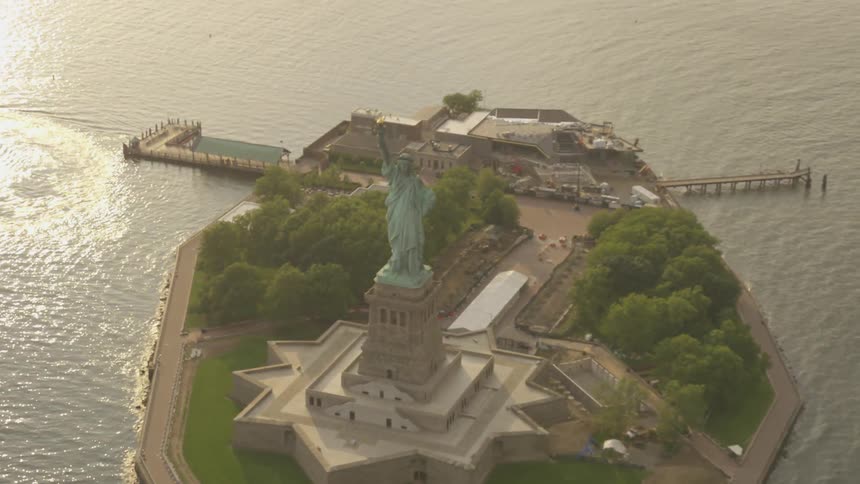 The statue of liberty stands atop her island on a bright sunny day