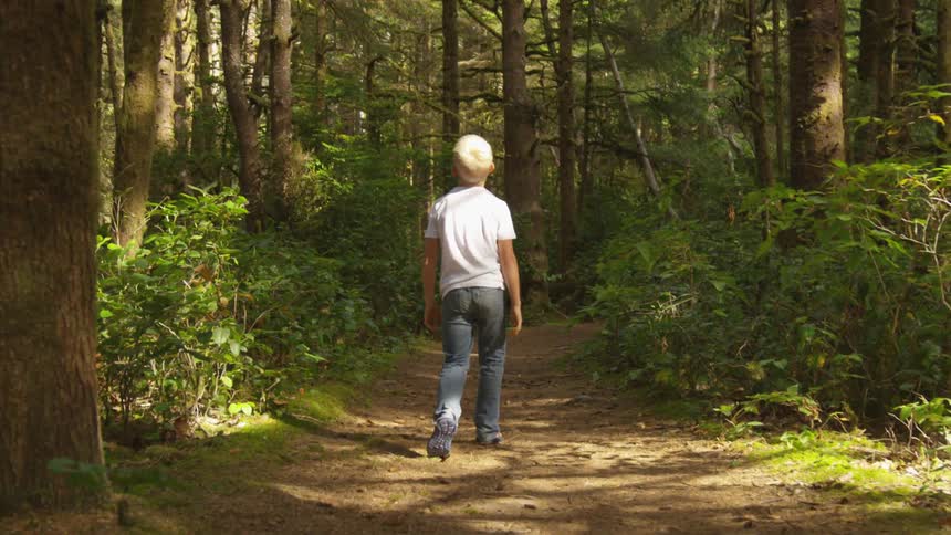 Boy walks on forest path looking around at dusk