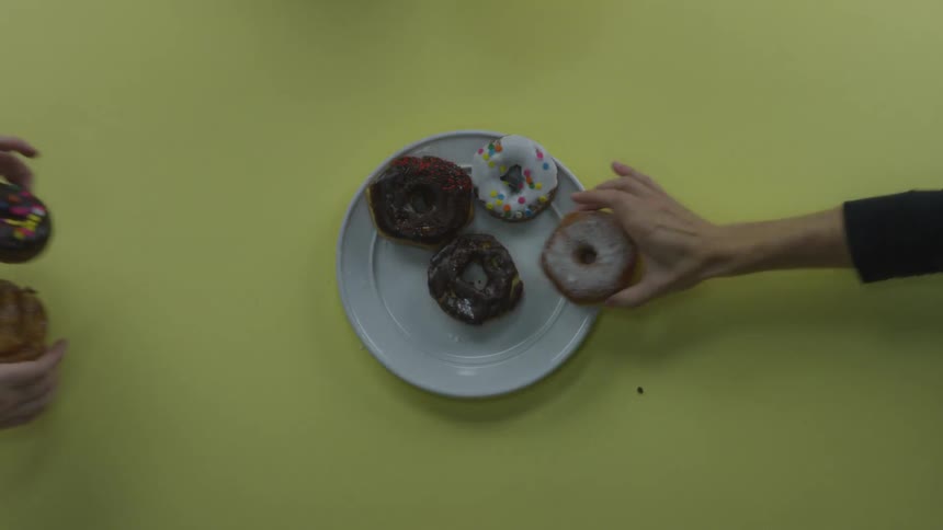 Lots of hands grab colorful donuts off of a plate