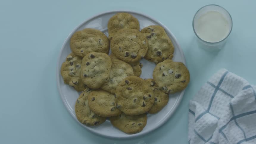 Cookies rest on a table as someone picks up one dips it in milk and takes a bite