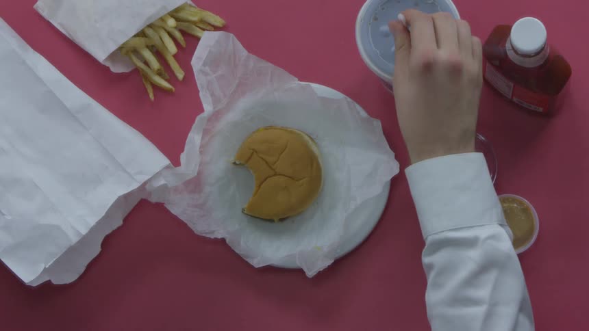 A person puts a straw in their drink cup and picks up the ketchup bottle next to their burger and fries