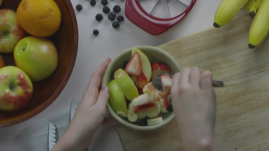 A person mixing some fruit in a bowl