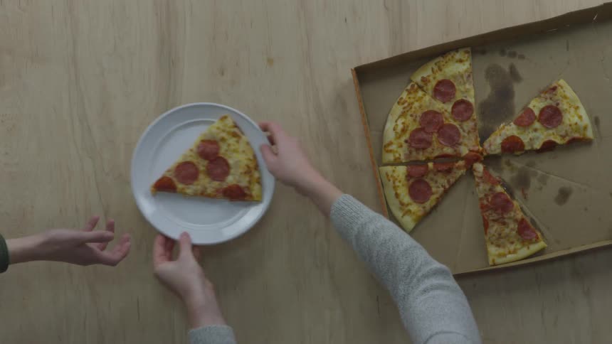 A person taking a slice of pizza from a box plating it and handing the plate to another person