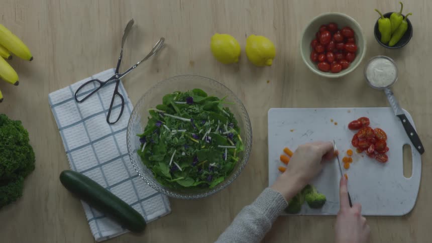 Person chops vegetables on chopping board laying on wooden table