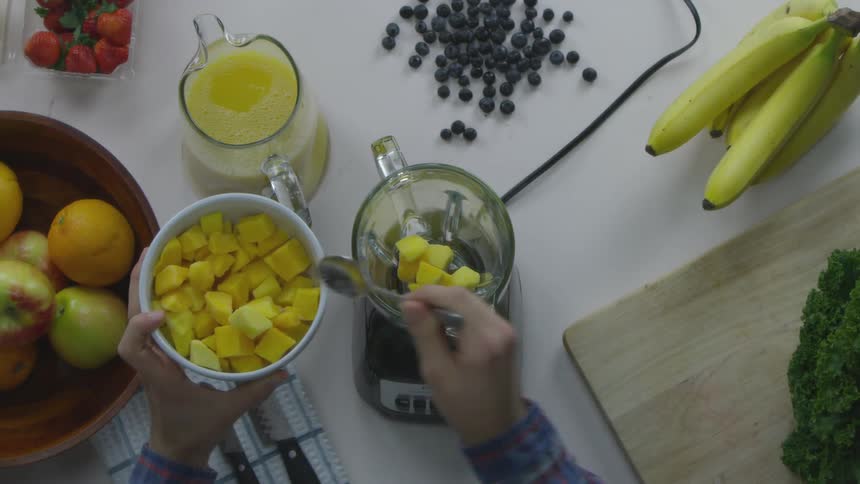 A man adds cubed fruit to a blender as he prepares a fruit and vegetable smoothie