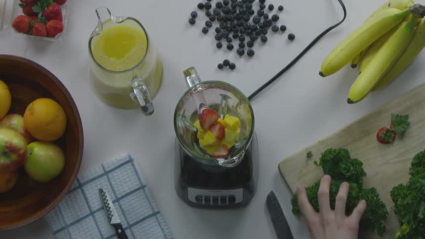 Person chopping kale placing in blender with fruit to make a smoothie