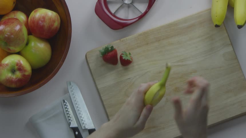 Woman peels banana on the cutting board in the kitchen by day