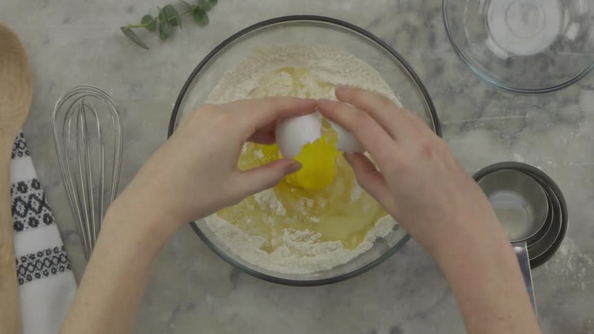 Chef cracks an egg into a glass bowl of ingredients
