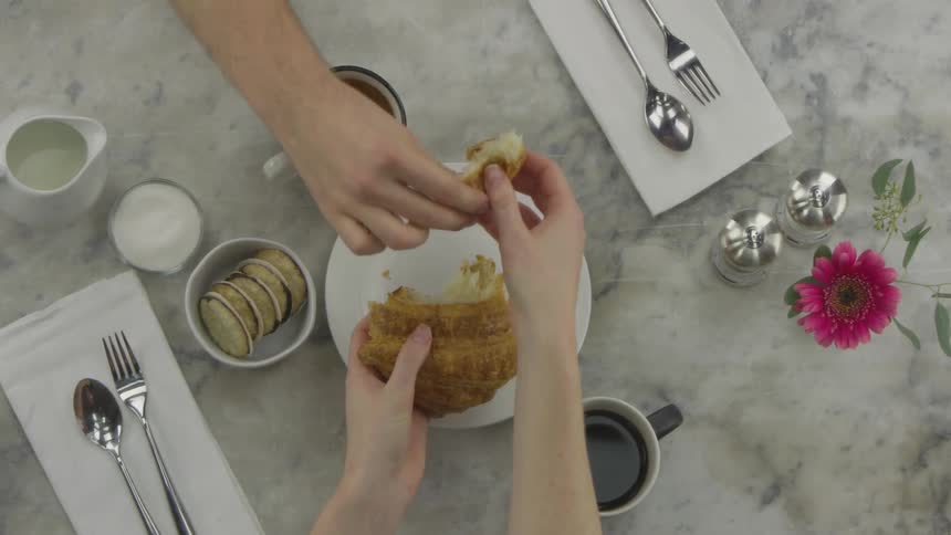 A table setting with food and drinks two people are sharing a croissant