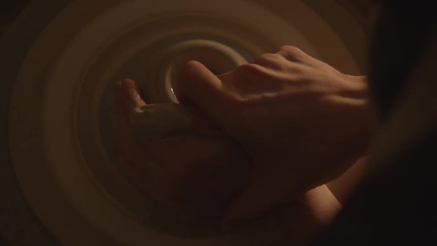 A potter's hands shape clay on a turning potters wheel