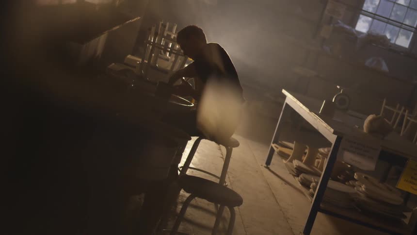Person sits on a stool and works a pottery wheel
