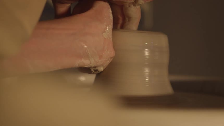 A white person shaping wet clay using a potter's wheel