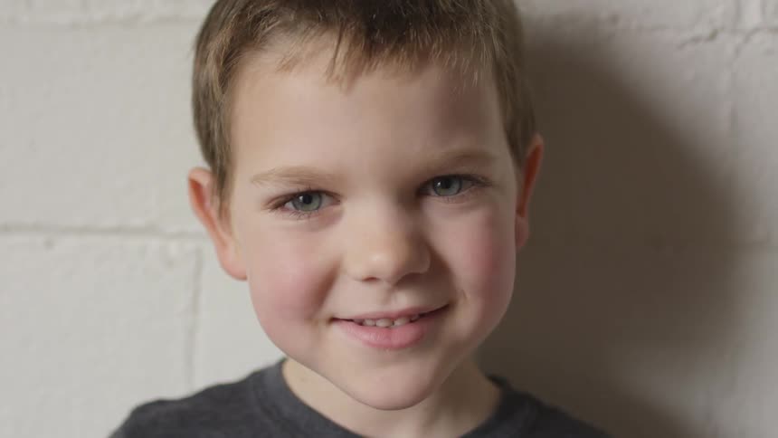 A young boy smiling while standing in front of a wall