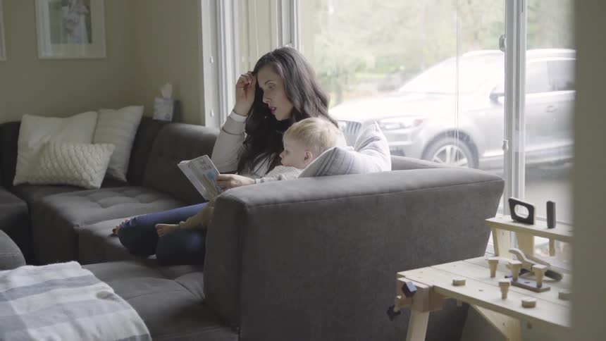 A young woman reads a story book to a blond toddler
