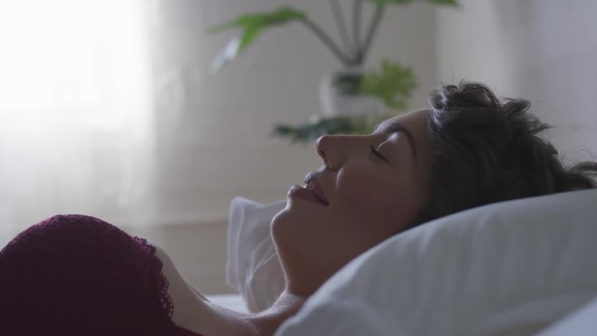 A woman and magenta underwear laying on a bed during the day
