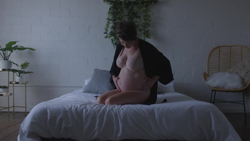 A pregnant woman sitting in a bed in lingerie