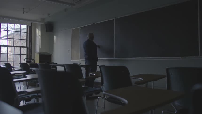 Man writing on the chalkboard in a classroom in the dark
