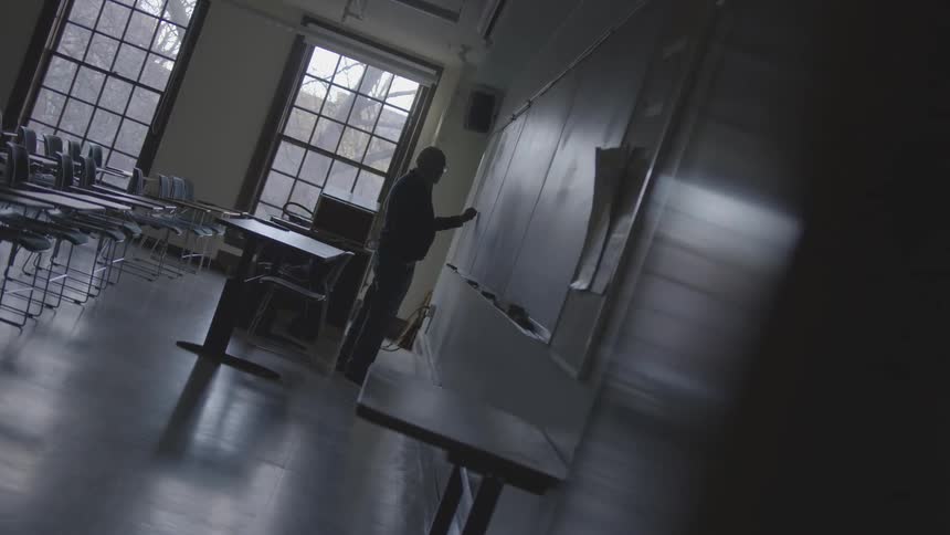 Man stands at blackboard in empty classroom