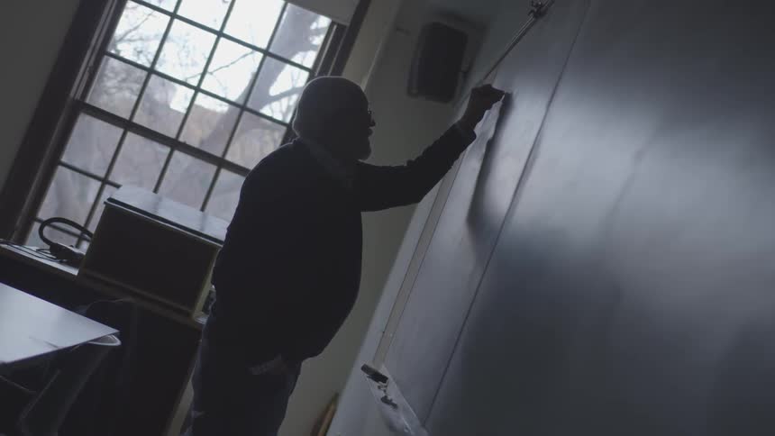 Elderly man writes on chalkboard