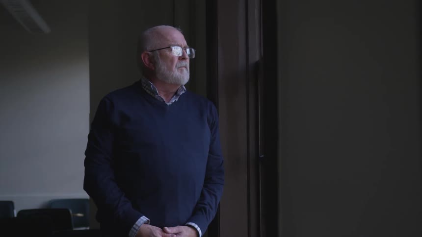Elderly man stares out a window from inside