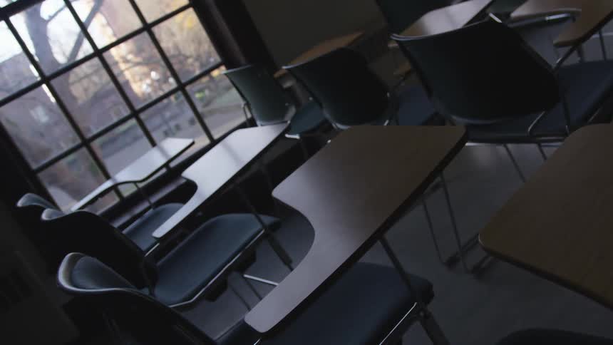 Desks with integrated chairs in an empty unlit classroom during the day