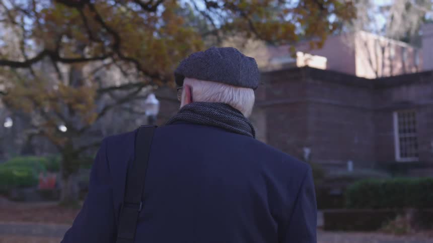 A man wearing a hat walking on a sidewalk