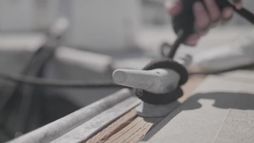 Person wearing white gloves untying rope from hook on a deck