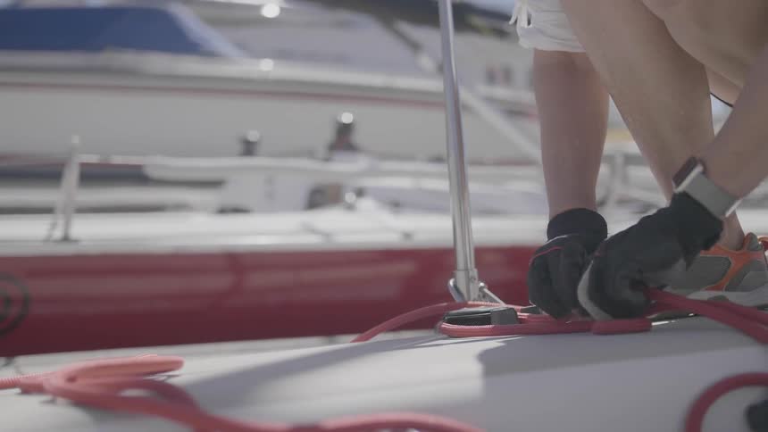A person squatting on a boat and pulling rope through a pulley