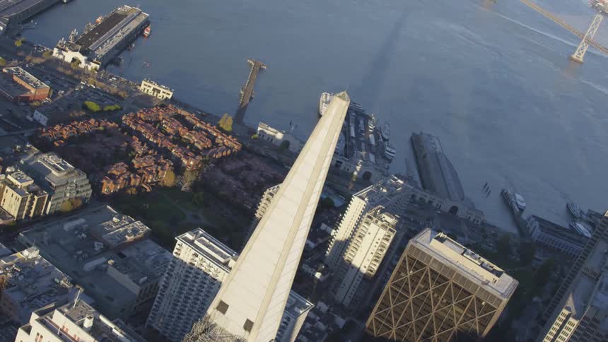 The camera flies over a dense city next to a body of water