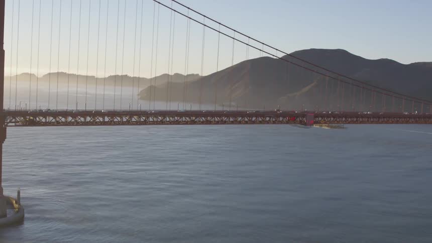 Cars cross suspension bridge with rocky mountain in background