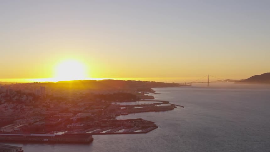 The sun sets on the horizon highlighting the coast line and a bridge