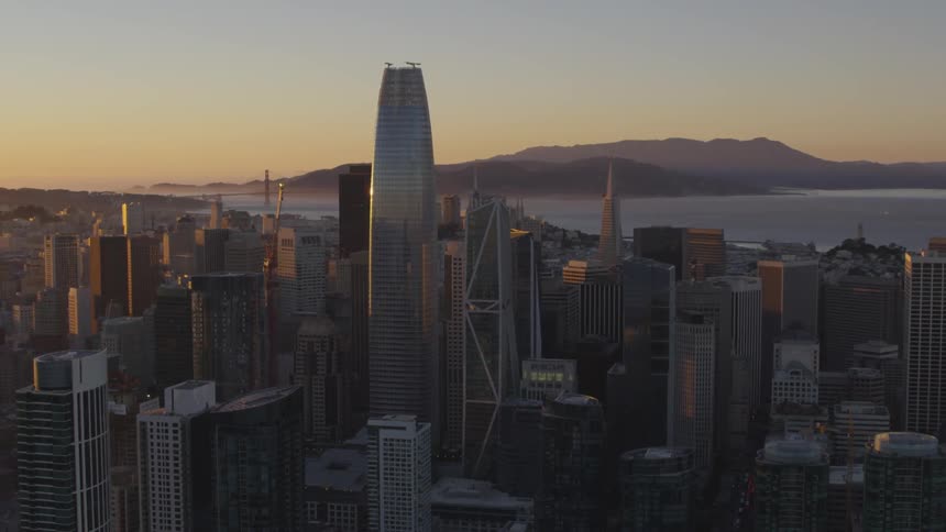 An aerial view of a large city at dawn with a body of water and mountains in the background
