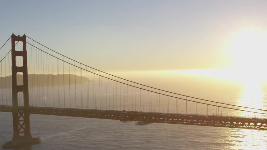 Traffic crosses suspension bridge over ocean as sun rises