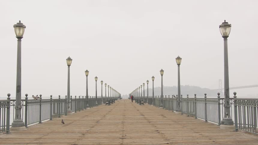 A person walking on a boardwalk that is over water and near mountains