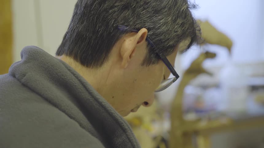 Elderly man in glasses looks down at something he's working on