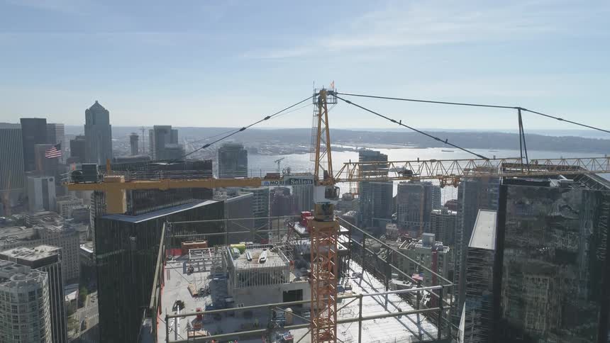 A tall crane stands in busy construction site in a scene of skyscrapers by a river