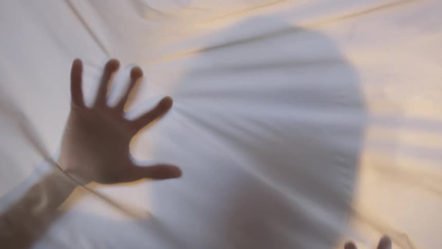 Backlit figure behind white sheet moves hands slowly across sheet
