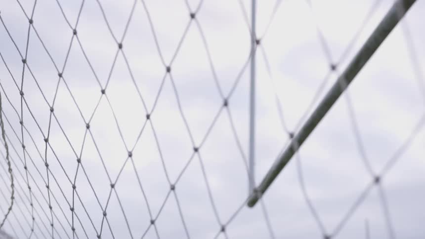 A soccer ball hits the back of the net under the football goal posts