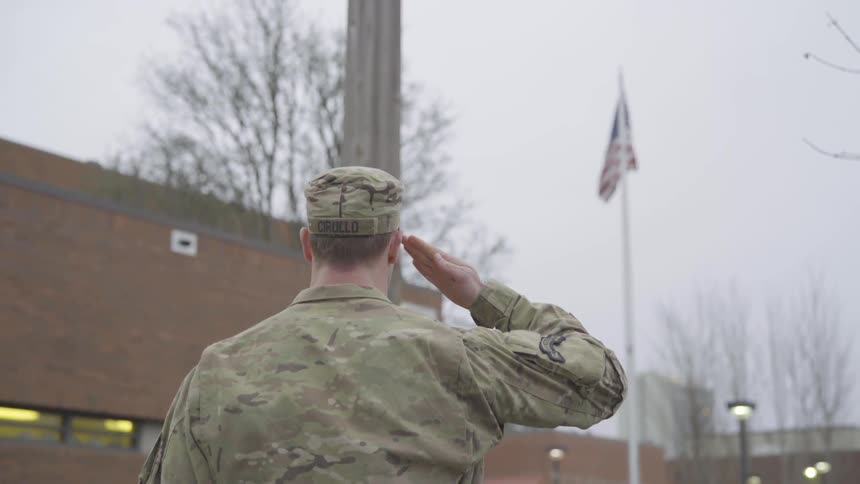 An army man is standing outside and saluting