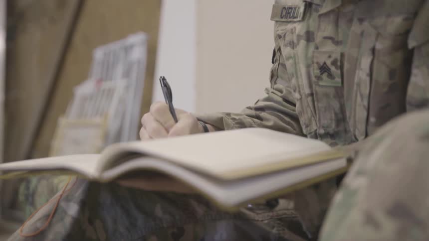 Soldier writes in a journal while sitting down inside a building