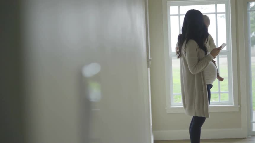 A pregnant woman standing in a room holding a baby