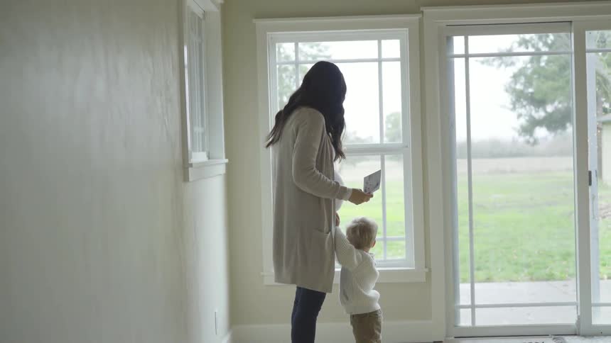 Pregnant woman holding paper stand in the corner looking down at toddler at house