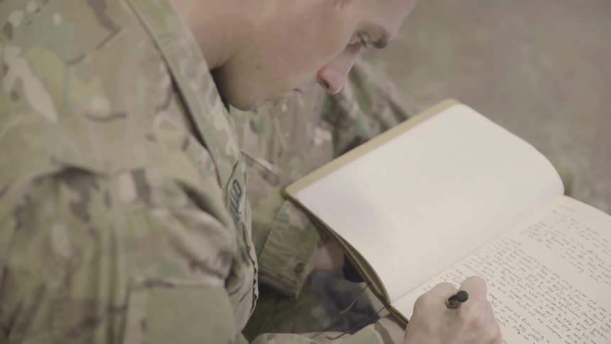 A seated soldier is looking down while writing in a journal