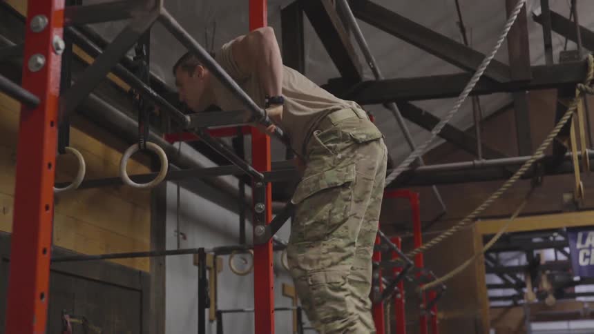 Male soldier does bar muscle ups in a gym