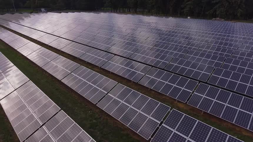 The camera flies over solar panels reflecting the sky