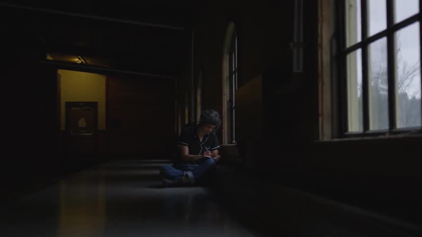 A person sits in shadows in front of a window
