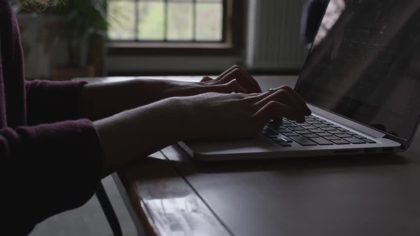 A person is sitting and typing on a laptop